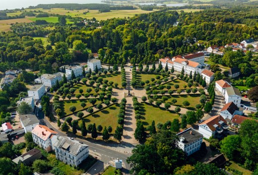 Widok z lotu ptaka na cyrk w Putbus na wyspie Rugia, okrągły plac z symetrycznie rozmieszczonymi drzewami i klasycystycznymi budynkami, otoczony zielenią i wiejskim krajobrazem.