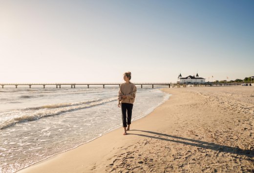 Wandelende vrouw op het strand van Ahlbeck bij zonsopgang met pier op de achtergrond
